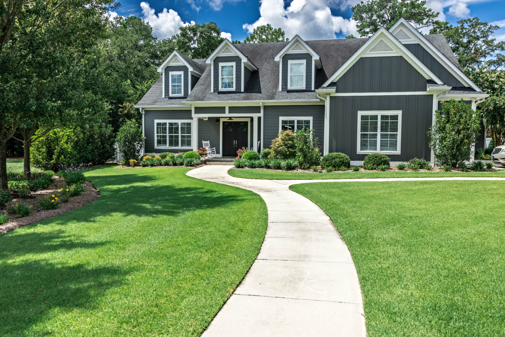 Modern gray house with professional landscaping featuring curved walkway, manicured lawn, and strategic plantings