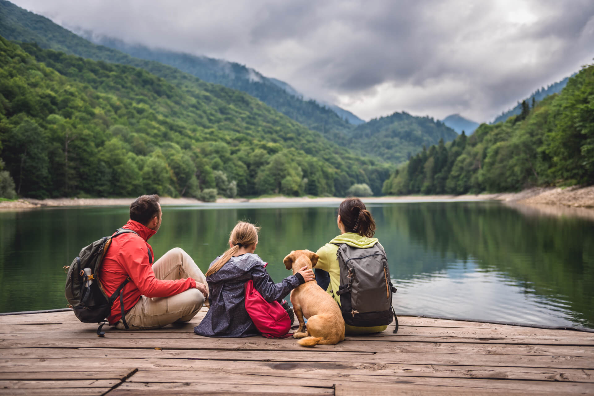 Family with their dog sitting on a dock by a mountain lake
